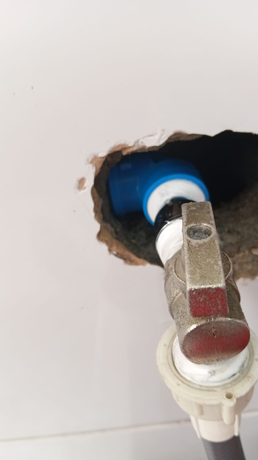 Parede aberta com tubulação azul e registro sendo instalado no ponto hidráulico