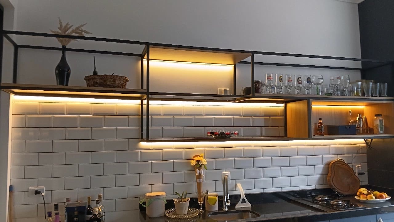 Prateleiras metálicas suspensas com iluminação em LED em parede de cozinha com azulejo branco