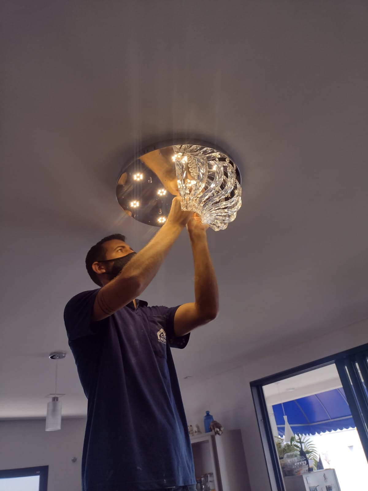Técnico instalando plafon de cristal no teto de uma sala