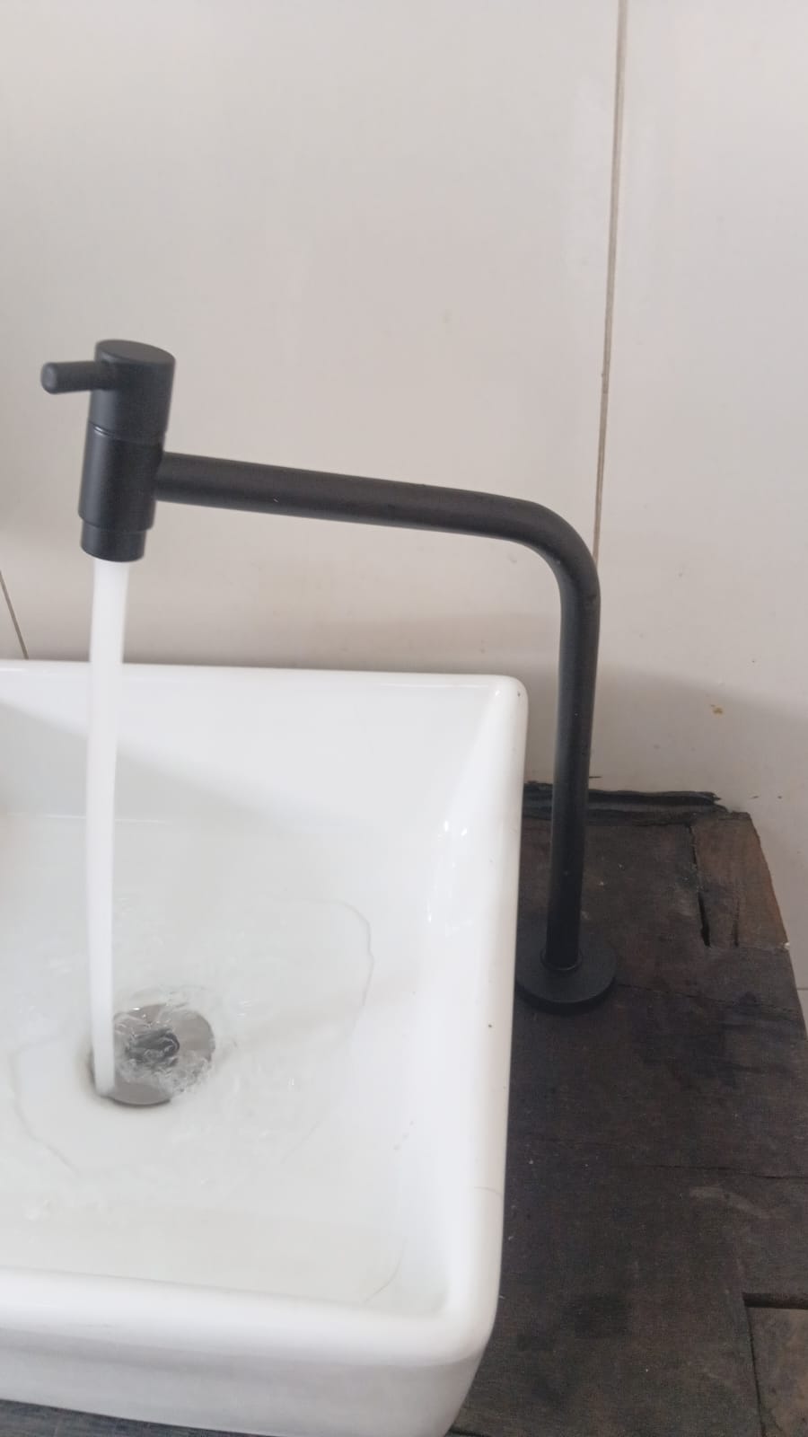 Torneira preta instalada em tanque com água corrente após o teste de vazão