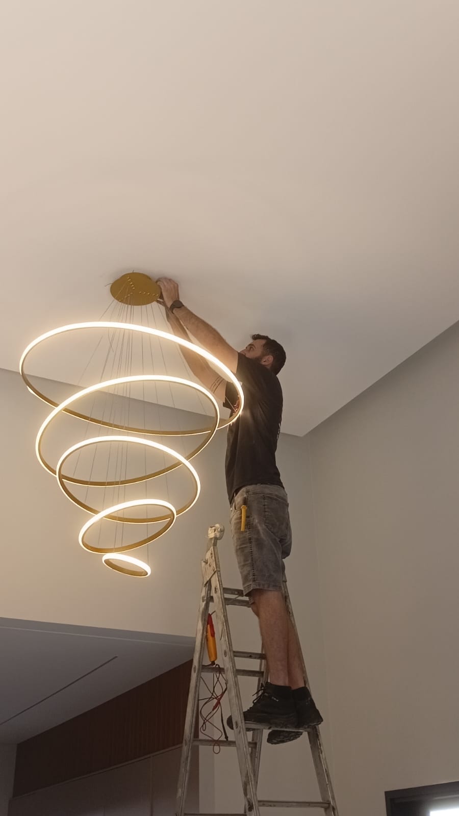 Técnico na escada instalando luminária de anéis em LED no teto